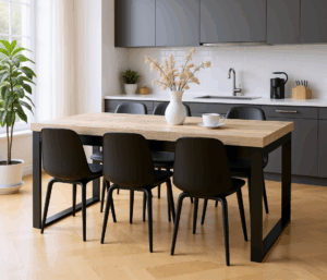 Nowoczesny stół z pogrubianym, jasnym blatem drewnopodobnym i czarnymi metalowymi nogami typu płoza, otoczony sześcioma czarnymi krzesłami, ustawiony w minimalistycznej kuchni z szarymi szafkami, jasną podłogą i dodatkami w postaci wazonu z kwiatami oraz roślin doniczkowych.