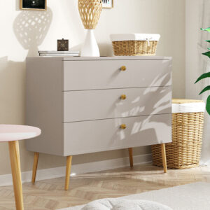 Stylowa komoda z trzema szufladami w kolorze kaszmir, na wysokich drewnianych nogach, w jasnym, nowoczesnym wnętrzu.