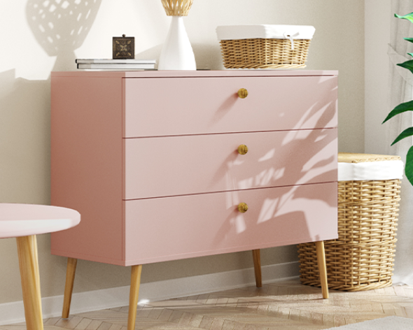 Komoda w stylu BOHO, róż naturalny, trzy szuflady, wysokie drewniane nogi, złote uchwyty, ustawiona w jasnym wnętrzu.